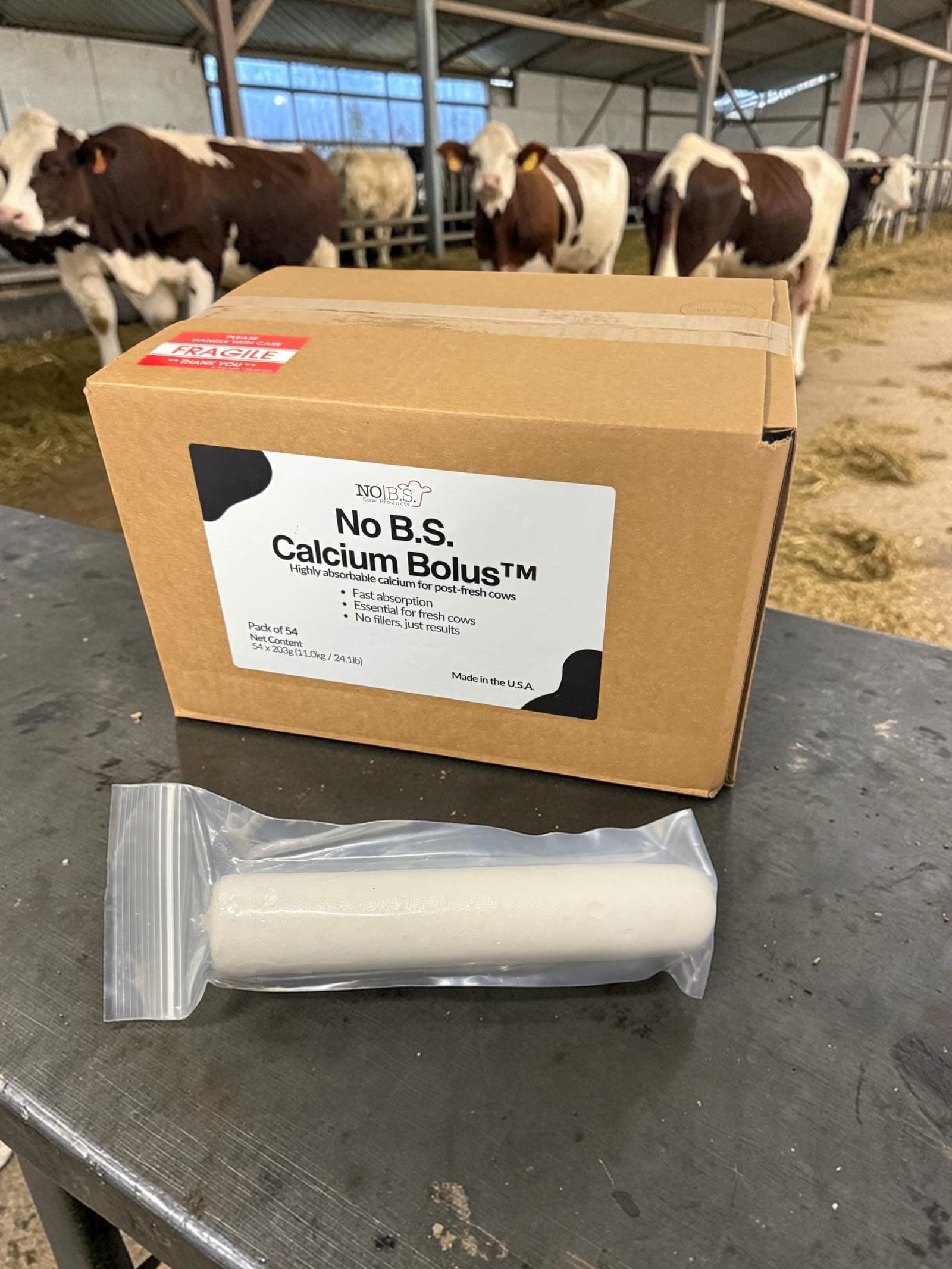 A case of No B.S. Calcium Bolus and a single sealed bolus on a table in front of fresh cows.
